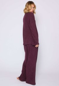 Conjunto de ropa de estar en burdeos hecho de un tejido de punto suave; presenta una parte superior de corte relajado con mangas largas y pantalones de pierna ancha.