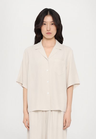 Lys beige kortærmet skjorte i et blødt materiale, med krave, knaplukning og en frontlomme. Enkelt, afslappet design.