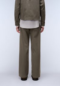 Μπεζ βαμβακερό μπουφάν πάνω από λευκό φανελάκι με ρίγες, συνδυασμένο με φαρδείς μπεζ παντελόνες και σκούρα παπούτσια, θέα από πίσω.