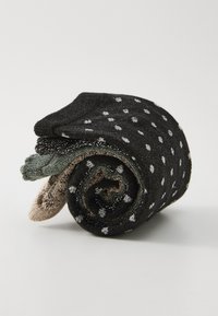 Calcetines de punto enrollados, con una base negra con lunares blancos, acentuados con verde, dorado y un acabado texturizado.