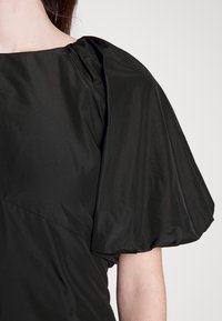 Top nero con maniche a sbuffo e scollatura quadrata. Il tessuto è liscio e il design presenta dettagli arricciati sulle spalle e una vestibilità aderente.