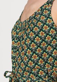 Svart klänning i tyg med grön, orange och vit blommönster. Har en rynkad halsringning och ett knytband i midjan för justering.