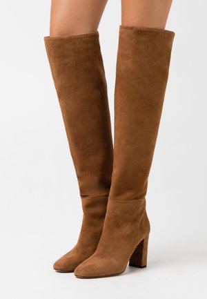 Botas de ante marrón por encima de la rodilla con punta cuadrada, tacón alto ancho y detalles mínimos de costura. Textura suave y diseño ajustado.