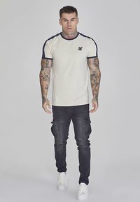 Kremfarvet T-shirt med korte ærmer og marineblå detaljer på kraven og ærmerne, stylet med mørke cargobukser og hvide sneakers.