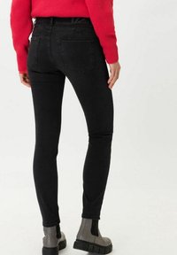Jeans skinny negros de denim, con una textura suave, cinturilla alta y bolsillos traseros. Llevados con botines grises hasta el tobillo.