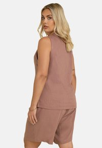 Top senza maniche color marrone chiaro con finitura texture abbinato a pantaloni corti leggeri coordinati. Vestibilità rilassata, design semplice e senza chiusure visibili.