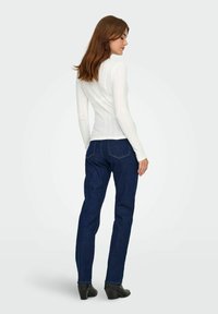 Vit ribbad långärmad topp matchad med mörkblå raka jeans och svarta klackstövlar, sedd bakifrån.