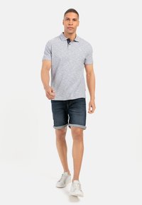 Polo shirt i lys grå med en mørkeblå krave, parret med opslåede mørke denim shorts og hvide sneakers, med en afslappet pasform.
