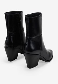 Botas de cuero negro hasta el tobillo con una forma elegante, cierre de cremallera y tacón grueso. Textura suave y detalles de costuras en la parte superior.