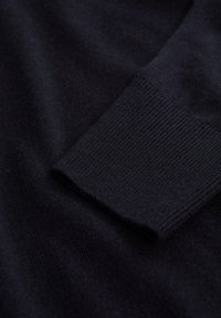 Mörk marinblå stickad tröjsärm med ribbad manschett, som visar den mjuka texturen av tyget.