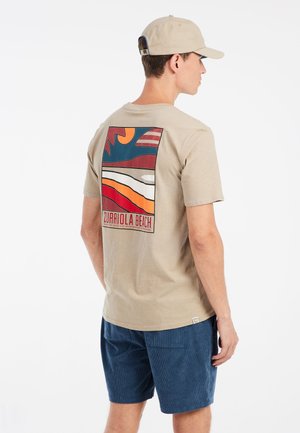 Camiseta beige con un diseño colorido en la parte trasera que presenta elementos de olas y sol; combinada con pantalones cortos de pana azul marino.