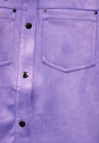 Chemise violette avec deux poches poitrine, boutons métalliques noirs et texture lisse. Les détails cousus mettent en valeur le design.