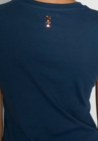 Bakåtsikt av en person som bär en marinblå skjorta med ett litet glänsande kopparfrågetecken och text nära nacken.