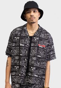 Black short-sleeve shirt with white cartoon panels featuring "Tom and Jerry" illustrations; includes a red logo on the chest.