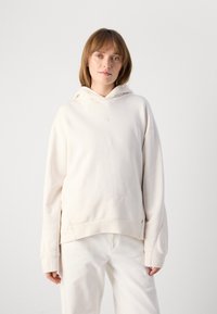 Cream hooded sweatshirt with a relaxed fit, featuring ribbed cuffs and hem, subtle logo detail on the chest, and soft cotton texture.