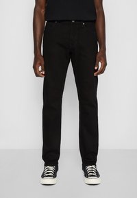 Vaqueros de mezclilla negra con corte recto, diseño de cinco bolsillos y herrajes de botones plateados, combinados con zapatillas negras y una camiseta negra.