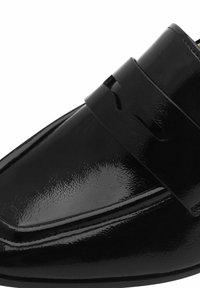 Svart lackläder loafer med spetsig tå, ett framträdande band över ovandelen och dekorativ utskärning. Glansig yta.