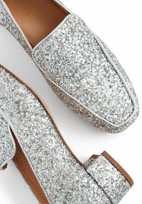 Stříbrné třpytivé loafers s hladkým koženým interiérem, čtveratou špičkou a nízkým blokovým podpatkem. Ozdobené bílým prošíváním podél okrajů.