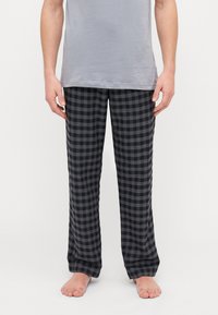 Pantalons de pyjama à carreaux noirs et gris en tissu doux, coupe ample avec des jambes droites et une taille confortable. Portés avec un T-shirt gris.