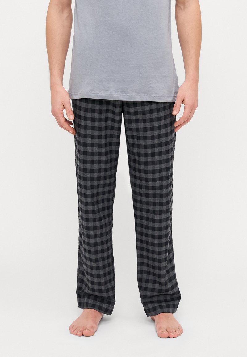 Pantalons de pyjama à carreaux noirs et gris en tissu doux, coupe ample avec des jambes droites et une taille confortable. Portés avec un T-shirt gris.