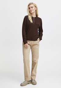 Brown zippered pullover with a chest pocket, paired with beige trousers and gray sneakers. The pullover has a casual fit and soft texture.