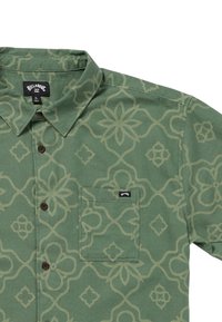 Grön mönstrad skjorta med krage, med en geometrisk blommig design och en bröstficka med en liten etikett.