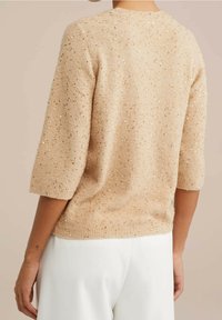 Beige kortärmad stickad tröja med glittriga guldaccenter, med en rund halsringning och en avslappnad passform. Texturen är mjuk med en subtil lyster.