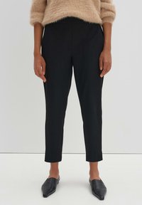 Pantalons noirs fuselés avec une texture lisse, dotés de poches latérales et d'une taille haute, associés à des ballerines noires pointues.