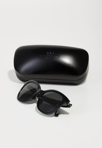 Lunettes de soleil noires avec une monture épaisse et des verres sombres, accompagnées d'un étui noir brillant avec un logo en relief.