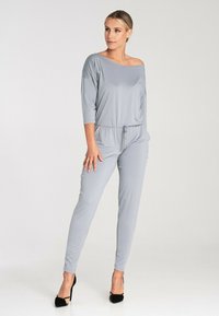 Szary kombinezon z off-shoulder, trzy czwarte rękawami, elastycznym pasem ze sznurkiem i zwężanymi nogawkami, wykonany z gładkiego, elastycznego materiału.