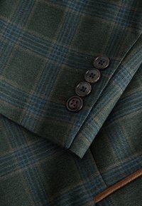 Dark green plaid jacket sleeve with four dark buttons and blue and brown check pattern.