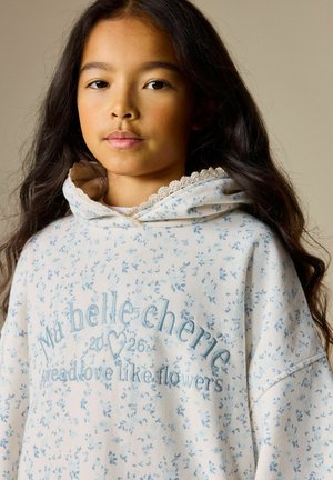 Krémově zbarvená mikina s kapucí s modrým květinovým vzorem, vyšívaným textem a krajkovým lemem na kapuci. Měkká tkanina a volný střih.