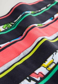 Ingrandimento di un tessuto piegato con strisce orizzontali nere, rosse e gialle sopra una stampa colorata in stile fumetto sottostante.