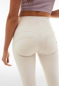 Leggings a vita alta di colore crema con una texture liscia, dotati di tasche posteriori curve e dettagli di cucitura a contrasto.