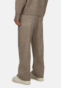 Brązowe dzianinowe spodnie o szerokiej nogawce, wykonane z miękkiego strukturalnego materiału, w zestawieniu z jasnymi sneakersami.
