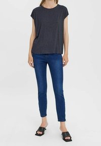 Tmavě šedé tričko s krátkým rukávem a volným střihem, spárované se slim-fit modrými džíny a černými sandály na otevřené špičce.