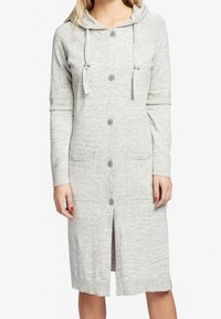 Femme portant un cardigan boutonné gris clair jusqu'aux genoux, avec une capuche, des manches longues et des poches avant.