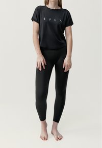 Zwart T-shirt met korte mouwen, voorzien van vier witte grafische accenten, gecombineerd met zwarte leggings met textuurpaneeltjes aan de zijkanten en een aansluitend ontwerp.