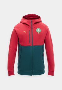 Rød og mørkegrøn hættetrøje med lynlås og hætte, Puma-logo på brystet og Marokkos fodboldforbunds emblem på venstre side.