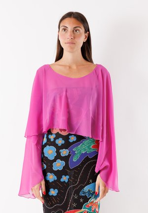 Blusa rosa trasparente con maniche lunghe e fluttuanti, design a strati, indossata sopra una gonna nera a motivi con motivi floreali colorati.