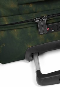 Grüner Rollkoffer aus strukturiertem Stoff, ausgestattet mit zwei Reißverschlüssen, einem Zahlenschloss und einem ausziehbaren Metallgriff.