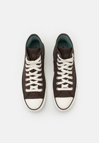 Bruine canvas sneakers met een witte rubberen neuskap, witte veters en een teal interieur. Heeft eenklassiek low-top ontwerp.