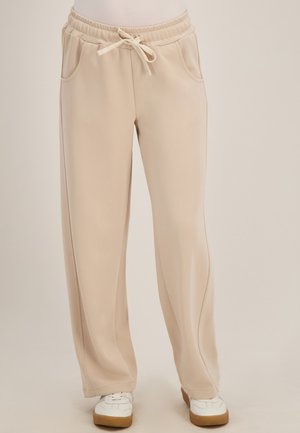 Beige sweatpants met wijde pijpen, elastische tailleband en trekkoord, gedragen met witte sneakers met bruine zolen.