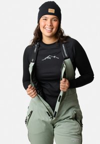 Vinteroverall i ljusgrön tyg med justerbara svarta remmar. Svart ribbad långärmad tröja med ett vitt bergsdesign.