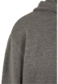 Grey knitted cardigan with a textured finish, featuring a hood and wide sleeves. The fabric appears soft and slightly fuzzy.