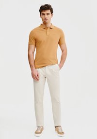 Beżowa koszulka polo, dopasowana, krótki rękaw, zestawiona z jasnobeżowymi spodniami i beżowymi trampkami. Minimalistyczny design, gładka tekstura.
