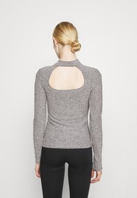 Long-sleeve top in a textured grey fabric with metallic flecks, featuring a cut-out back design and a high collar. Fitted style.