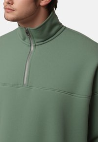 Pull-over vert à fermeture éclair quart, fabriqué en tissu texturé. Il présente un col montant et une fermeture éclair argentée pour un look moderne et décontracté.