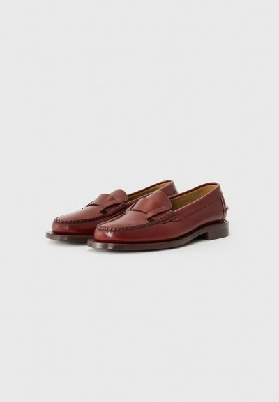 Braune Lederloafers mit einem geflochtenen Design auf dem Oberteil, einer glatten Oberfläche und einem gestapelten Holzabsatz. Sie besitzen eine abgerundete Zehenpartie und dezente Nähte.