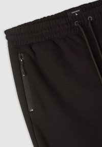 Pantaloni della tuta neri con vita elastica e coulisse regolabile. Tasca laterale con zip e tessuto morbido e strutturato per il massimo comfort.